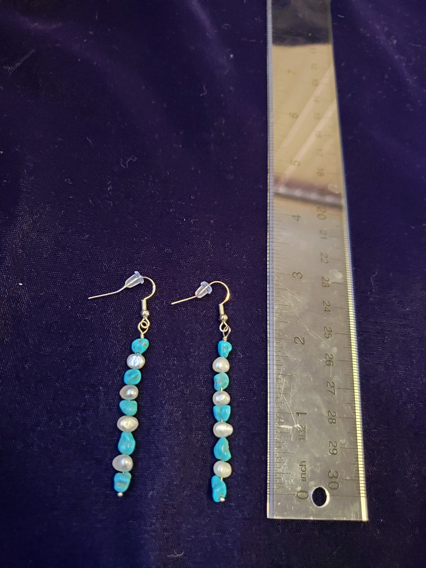 Pair of beaded earrings on a purple velvet background with a ruler for scale.