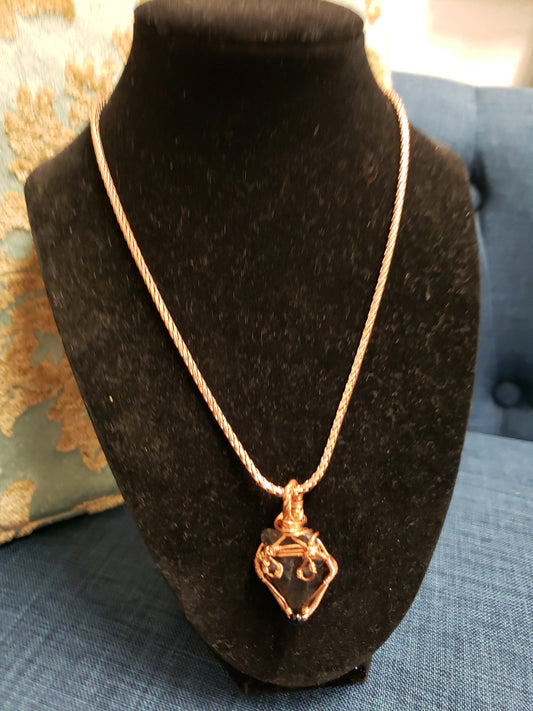 Copper necklace with a pendant on a black bust against a blue fabric background