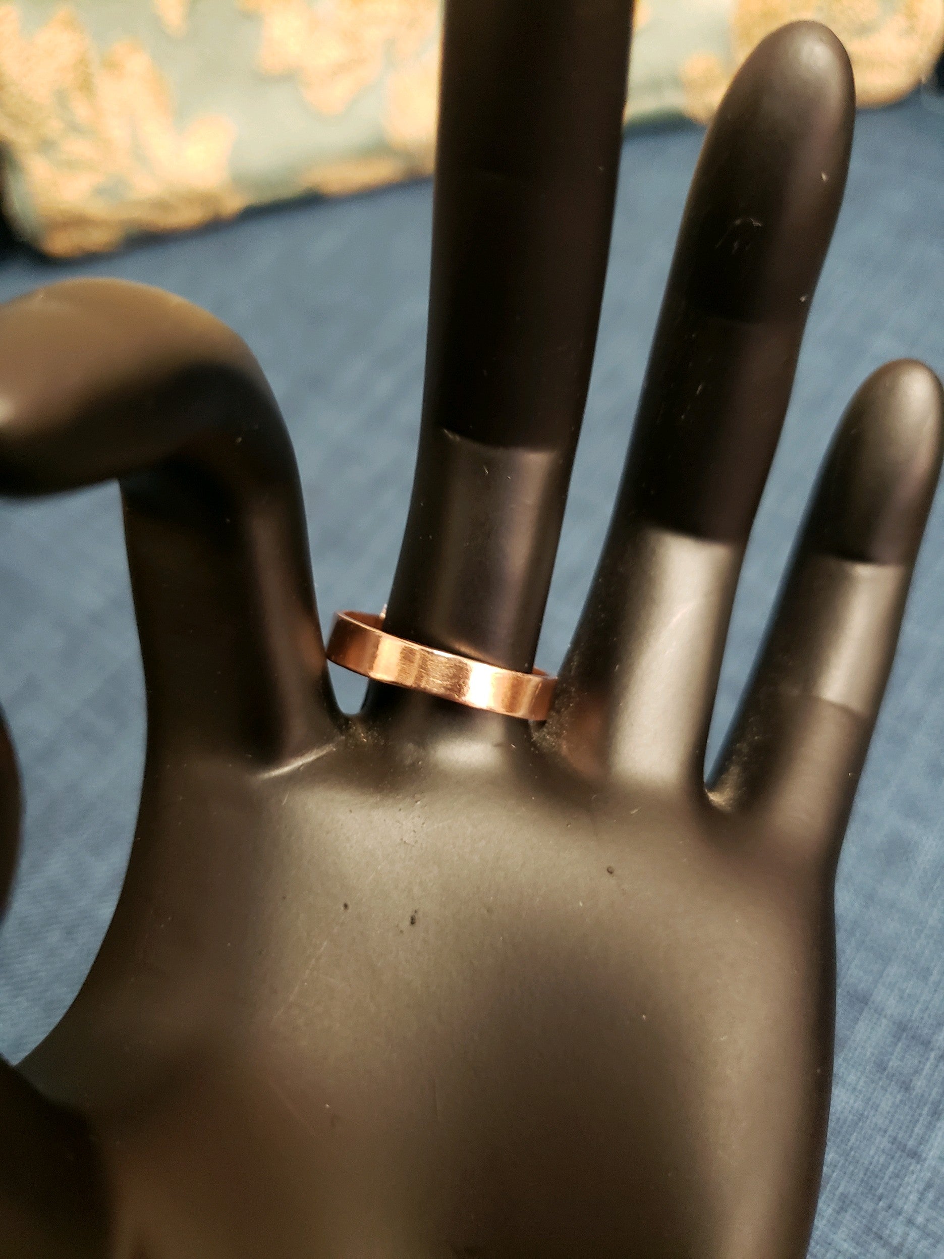Copper ring on a black mannequin hand against a blue background