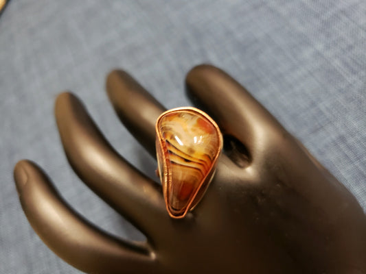 Ring with a large, orange-brown stone on a mannequin hand against a gray background