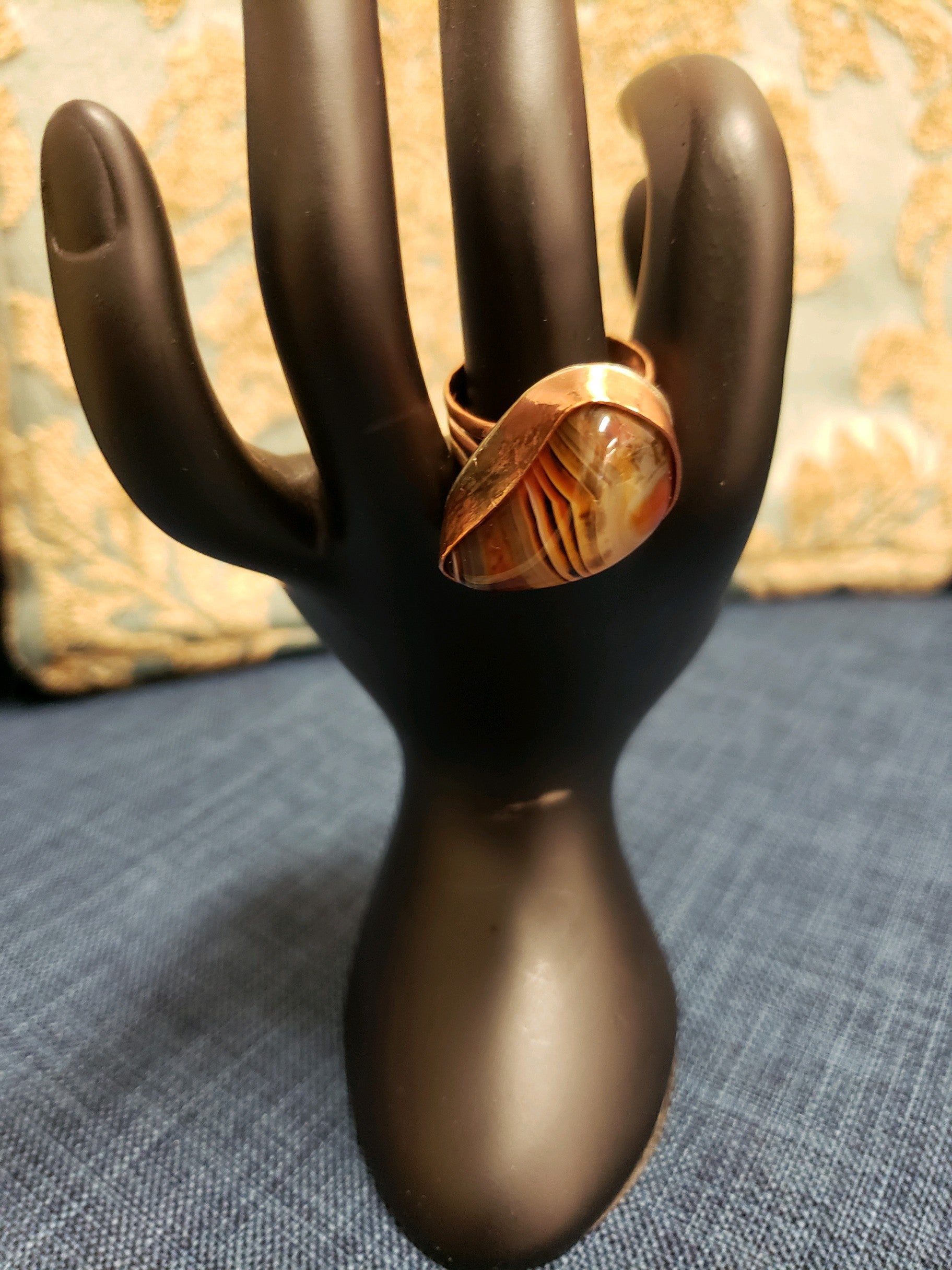 Mannequin hand holding a ring with a textured band on a textured surface