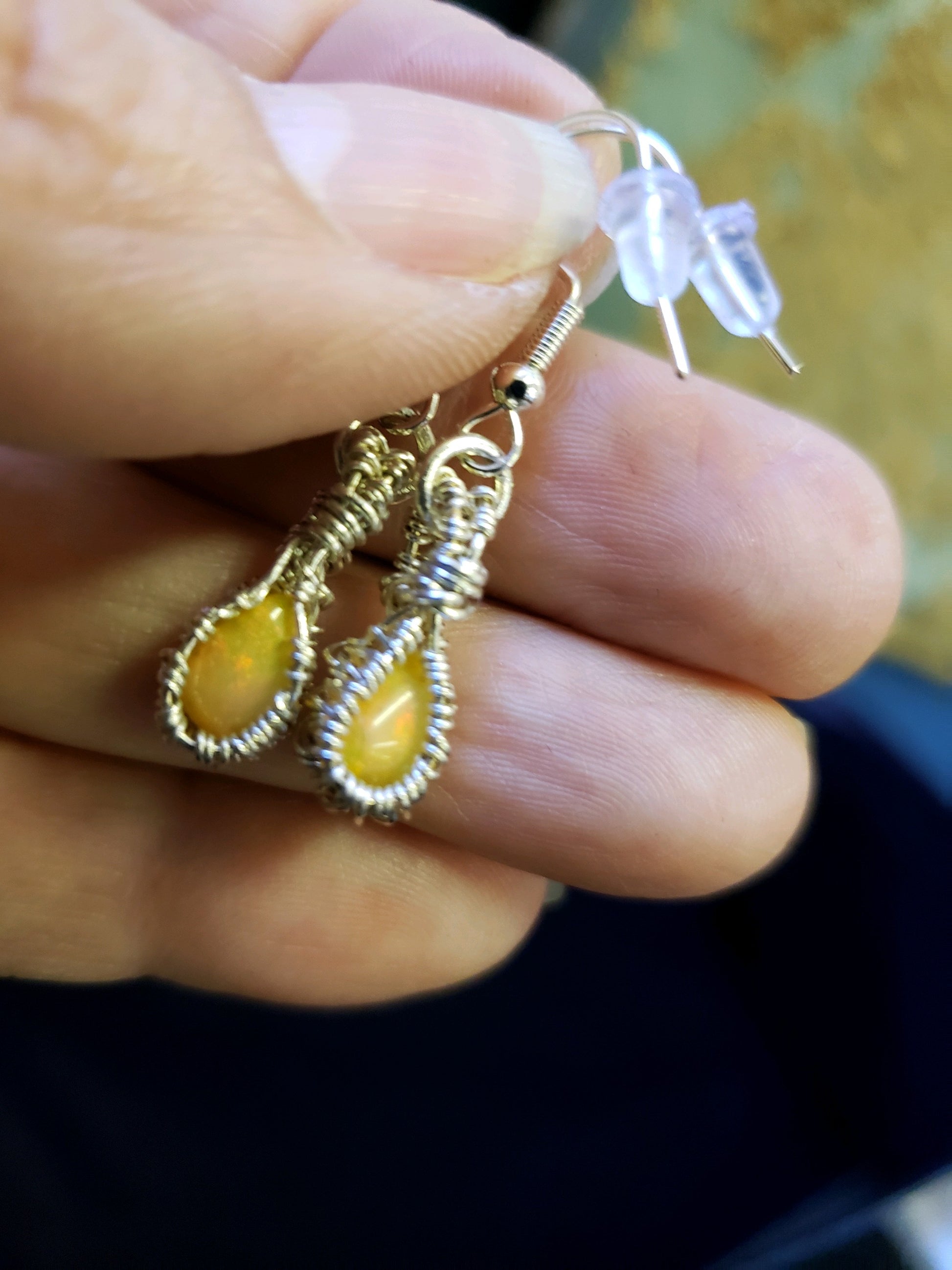 Earrings with yellow stones held between fingers against a blurred background