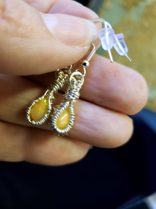 Earrings with yellow stones held between fingers against a blurred background