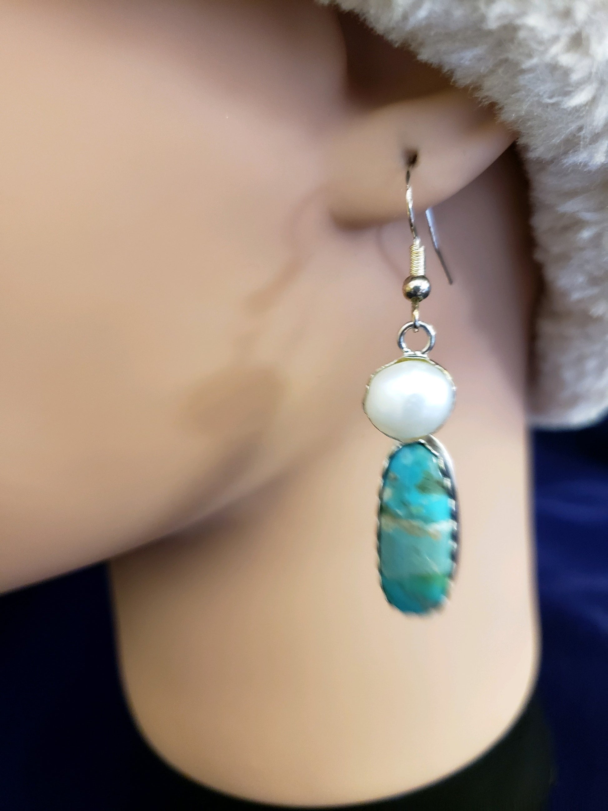 Close-up of an earring with a turquoise stone and pearl on a blurred background