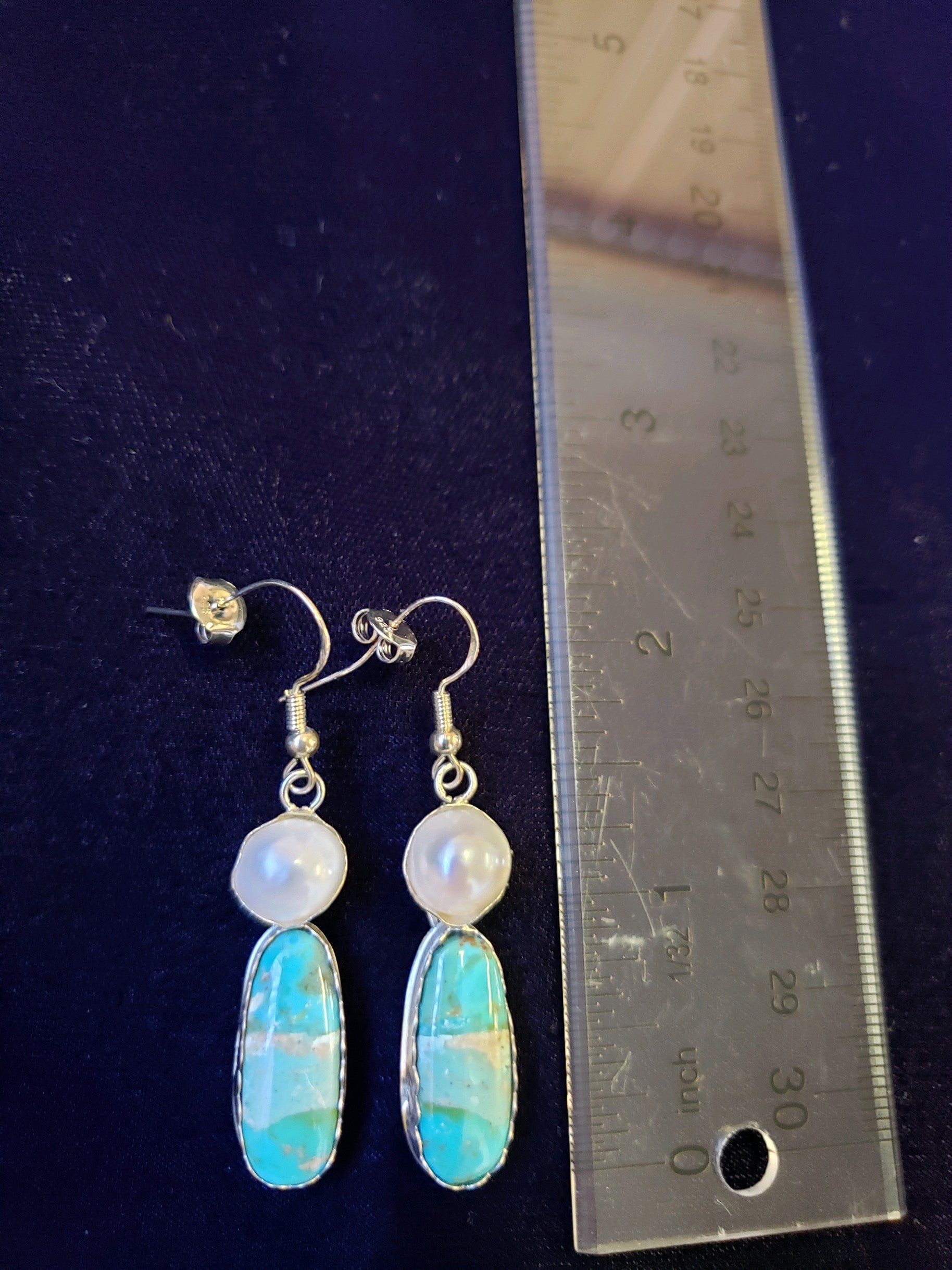 Opal and pearl earrings with a ruler for scale on a dark background