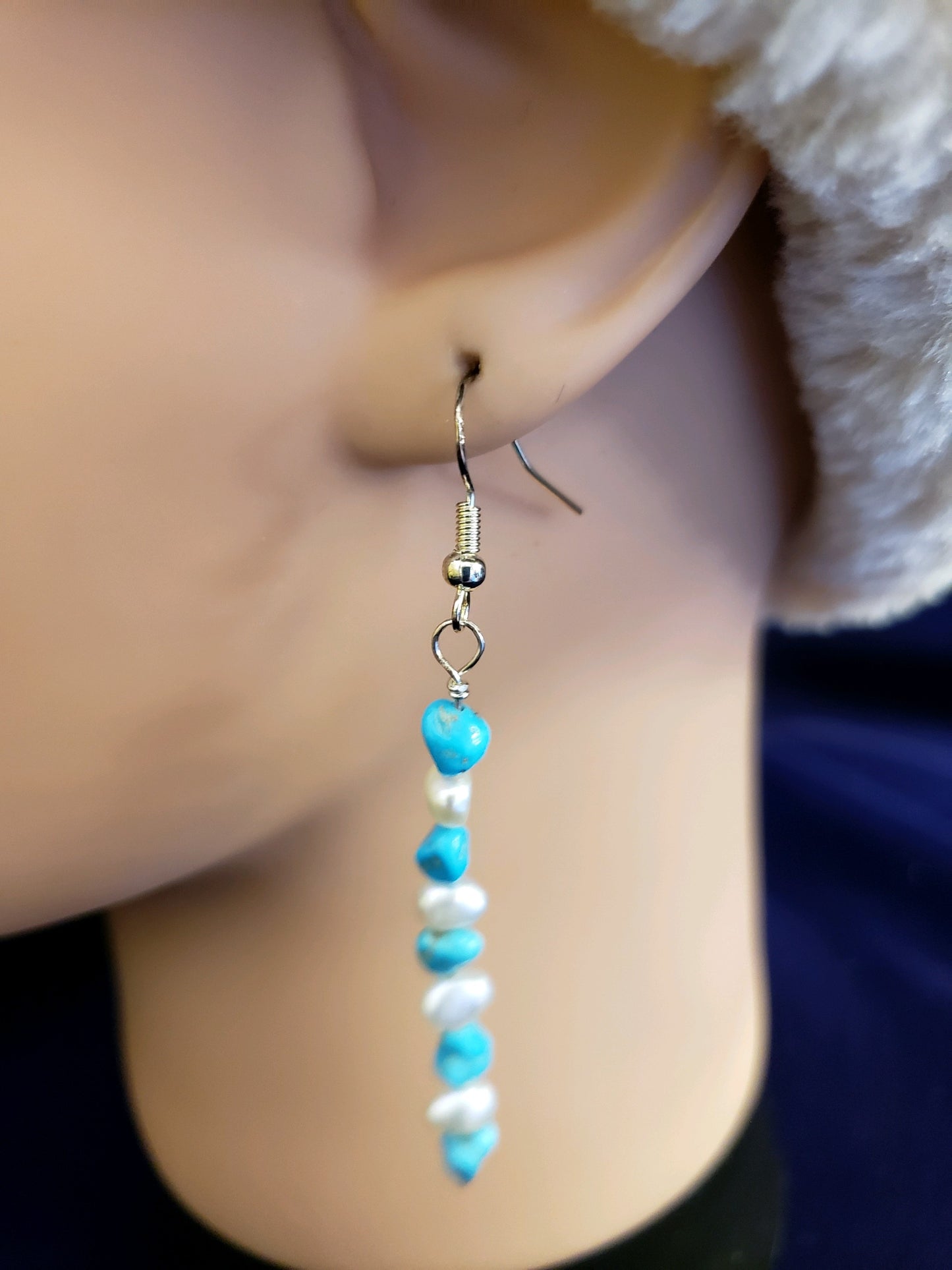 Earring with turquoise and pearl beads worn on a mannequin ear.