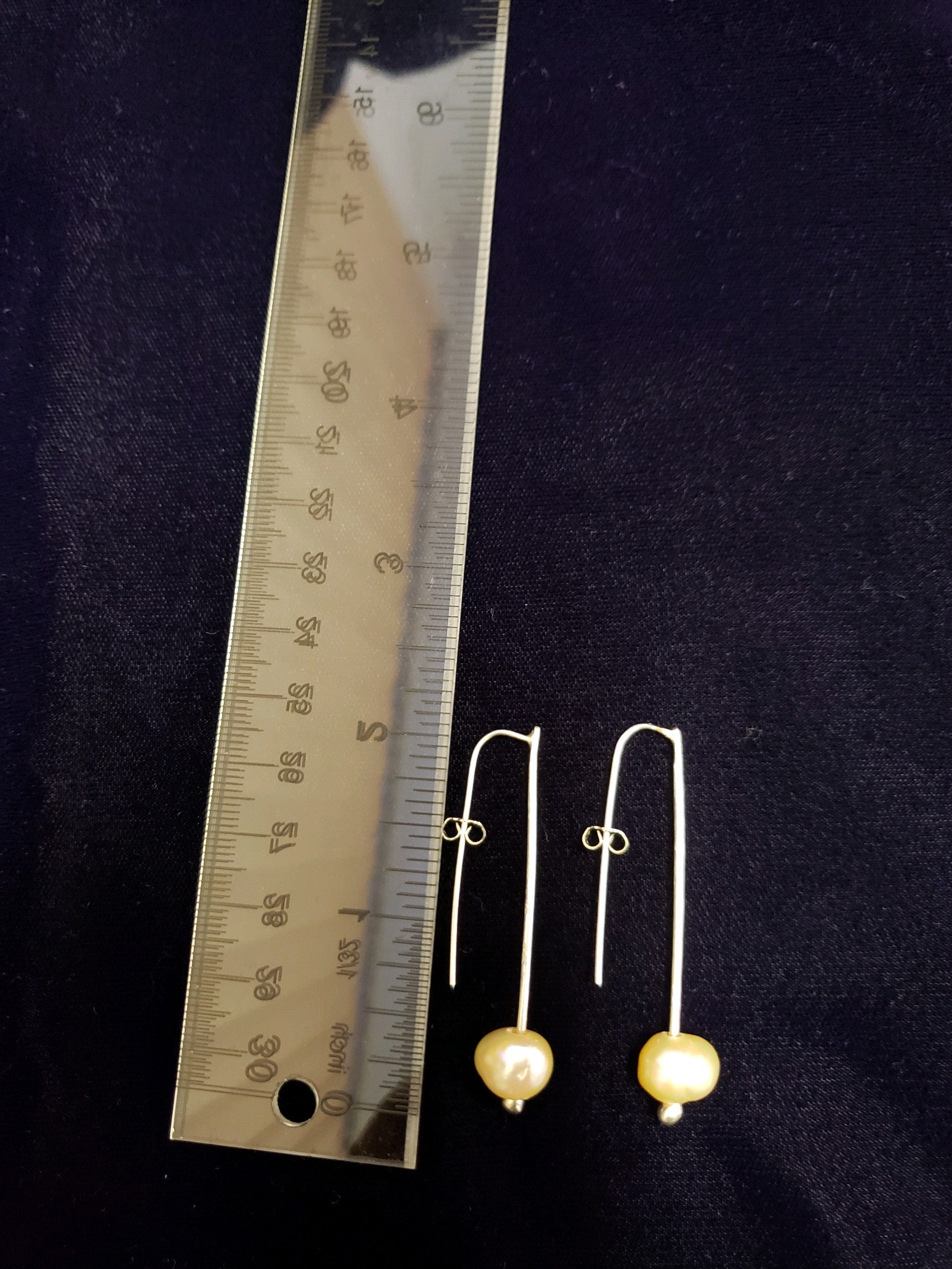 Pair of pearl earrings with a ruler for scale on a dark background