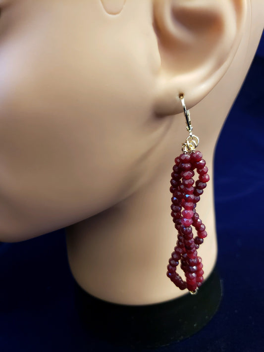 Red beaded earrings on a mannequin ear against a dark background
