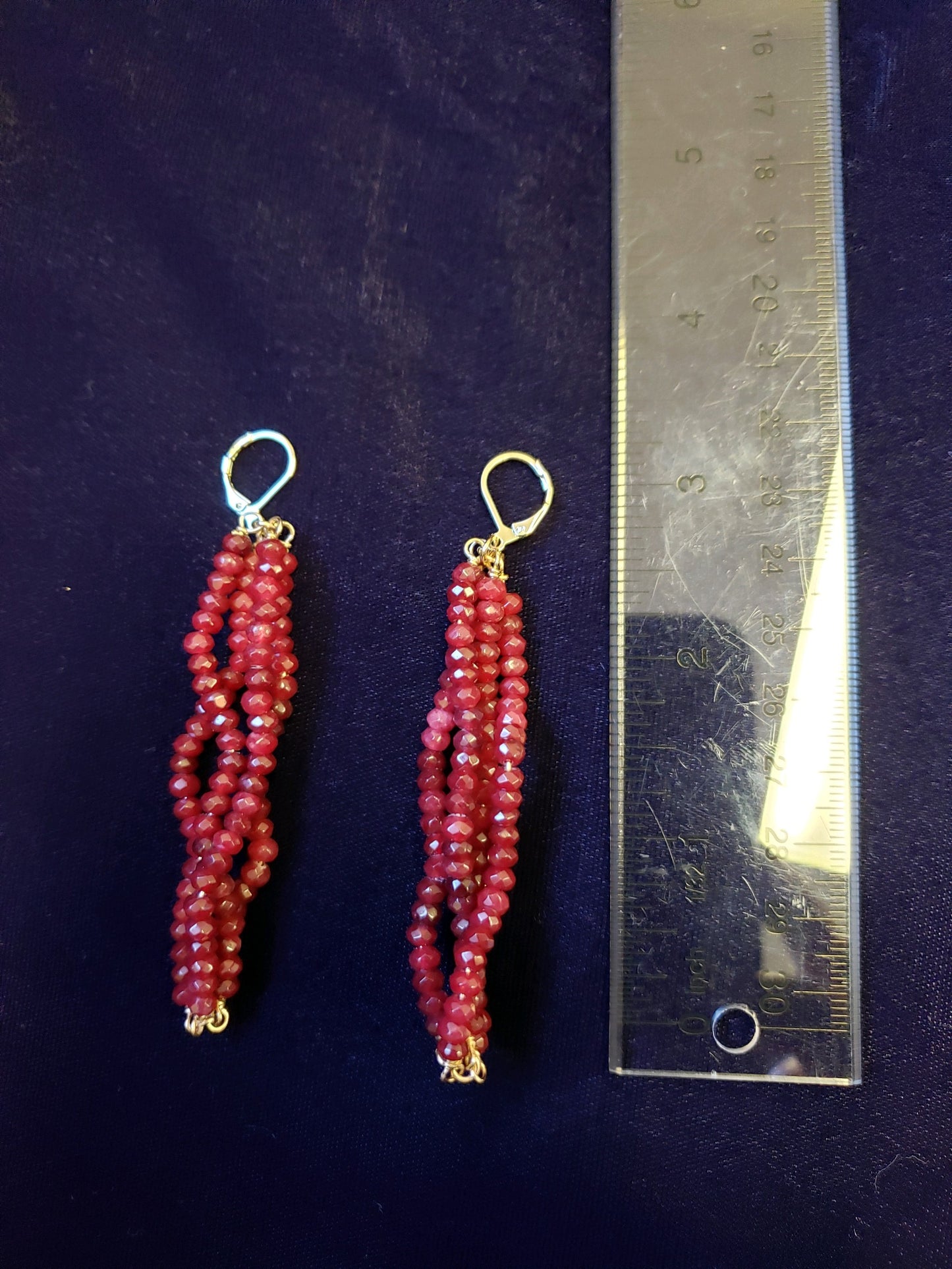Red beaded earrings with gold accents on a dark blue background with a ruler for scale.