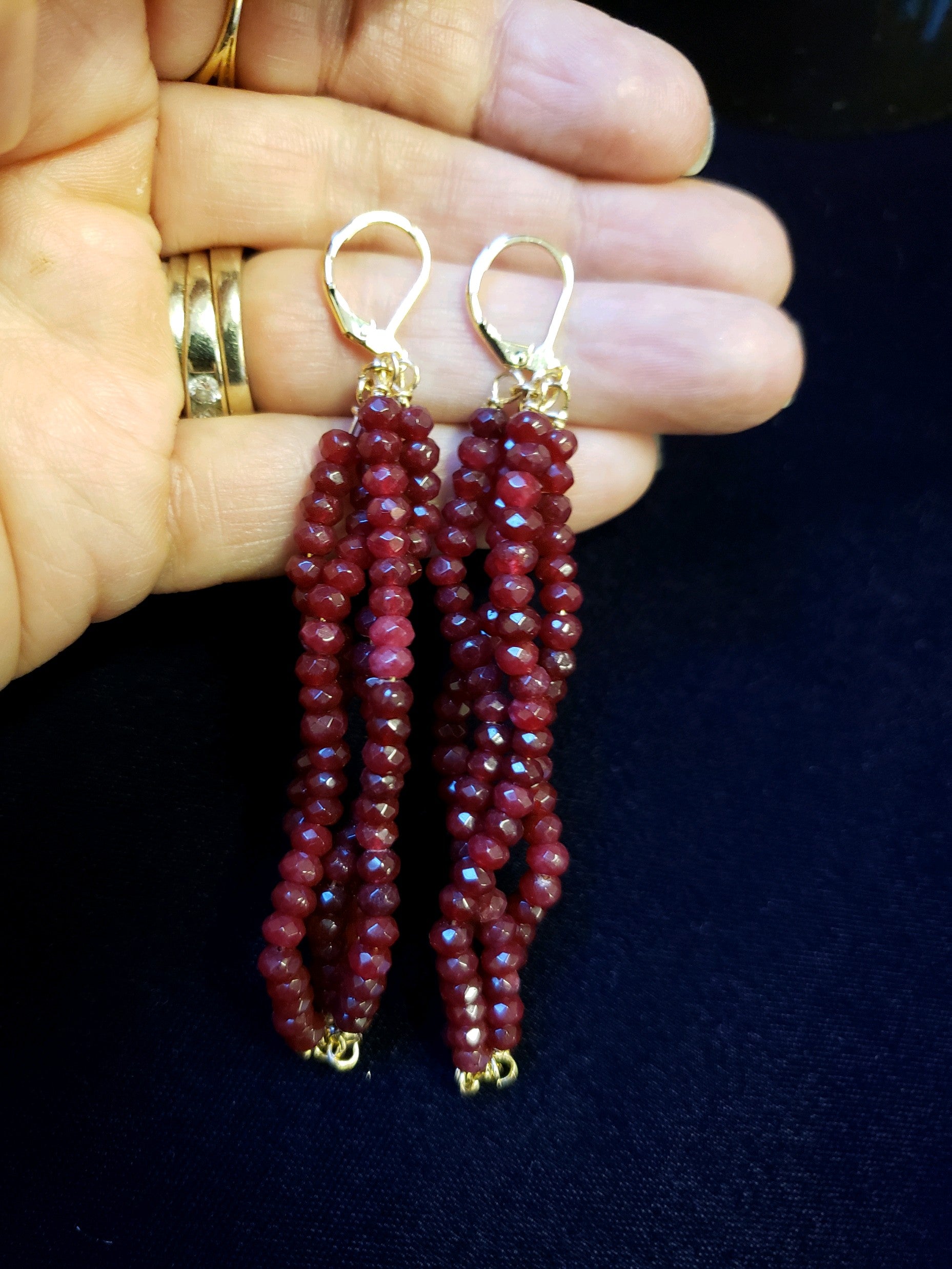 Burgundy beaded earrings held between fingers against a dark background