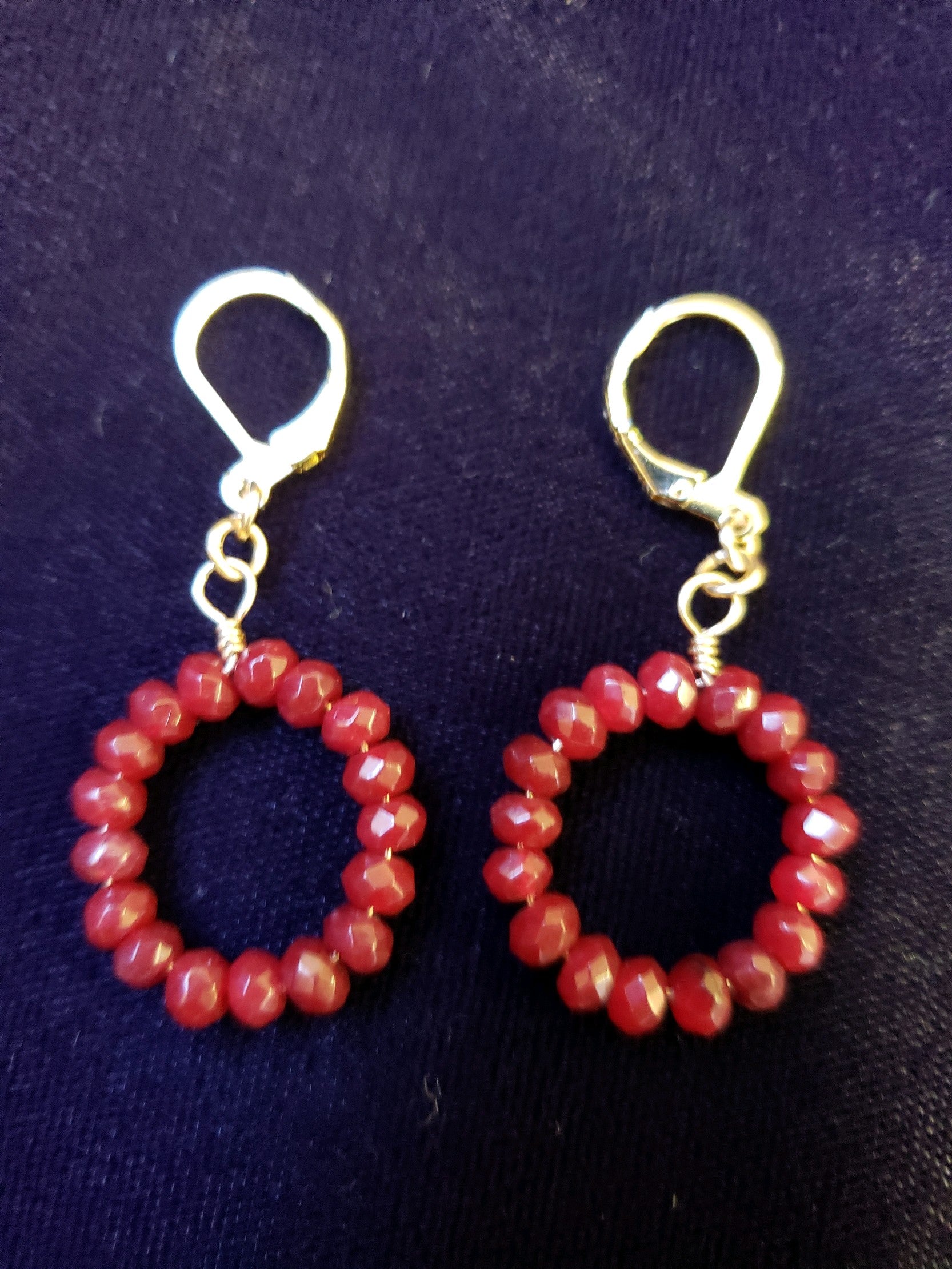 Pair of red beaded hoop earrings with gold clasps on a dark background