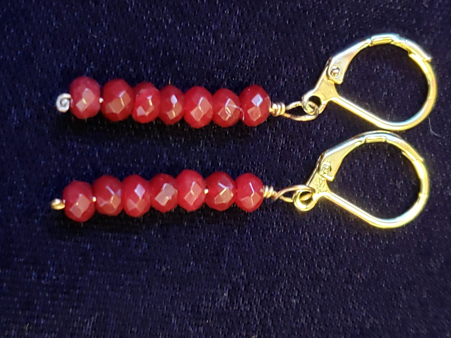 Pair of red beaded earrings with gold hooks on a dark background