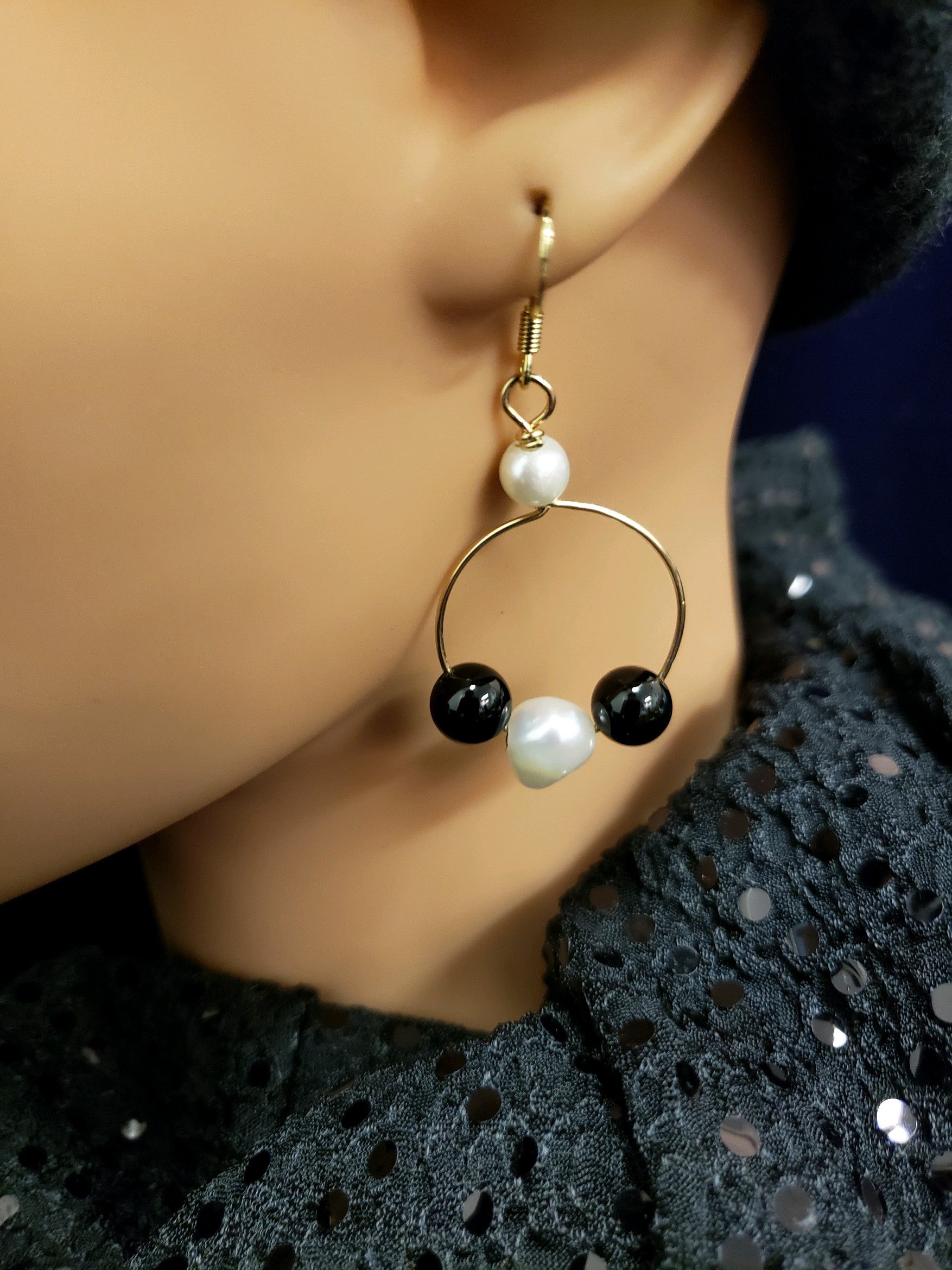 Earring with gold hoop, black bead, and pearl. 