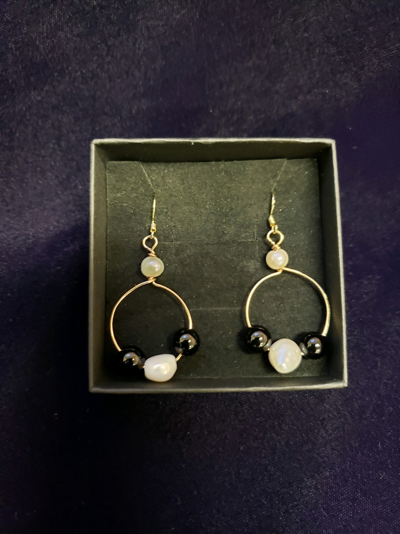 Pair of gold hoop earrings with pearls and black beads in a box on a dark background