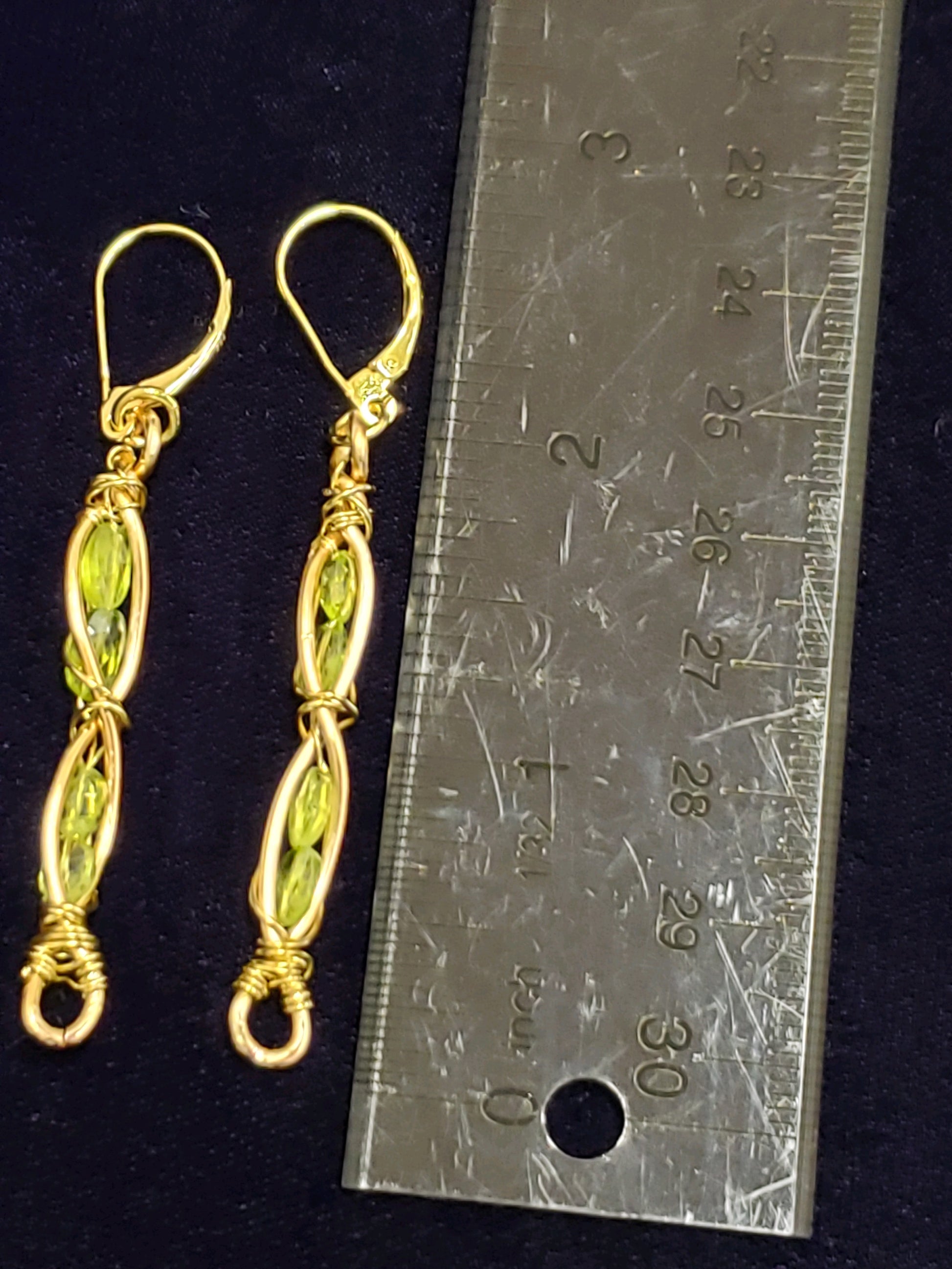 Gold earrings with green stones next to a ruler on a black background