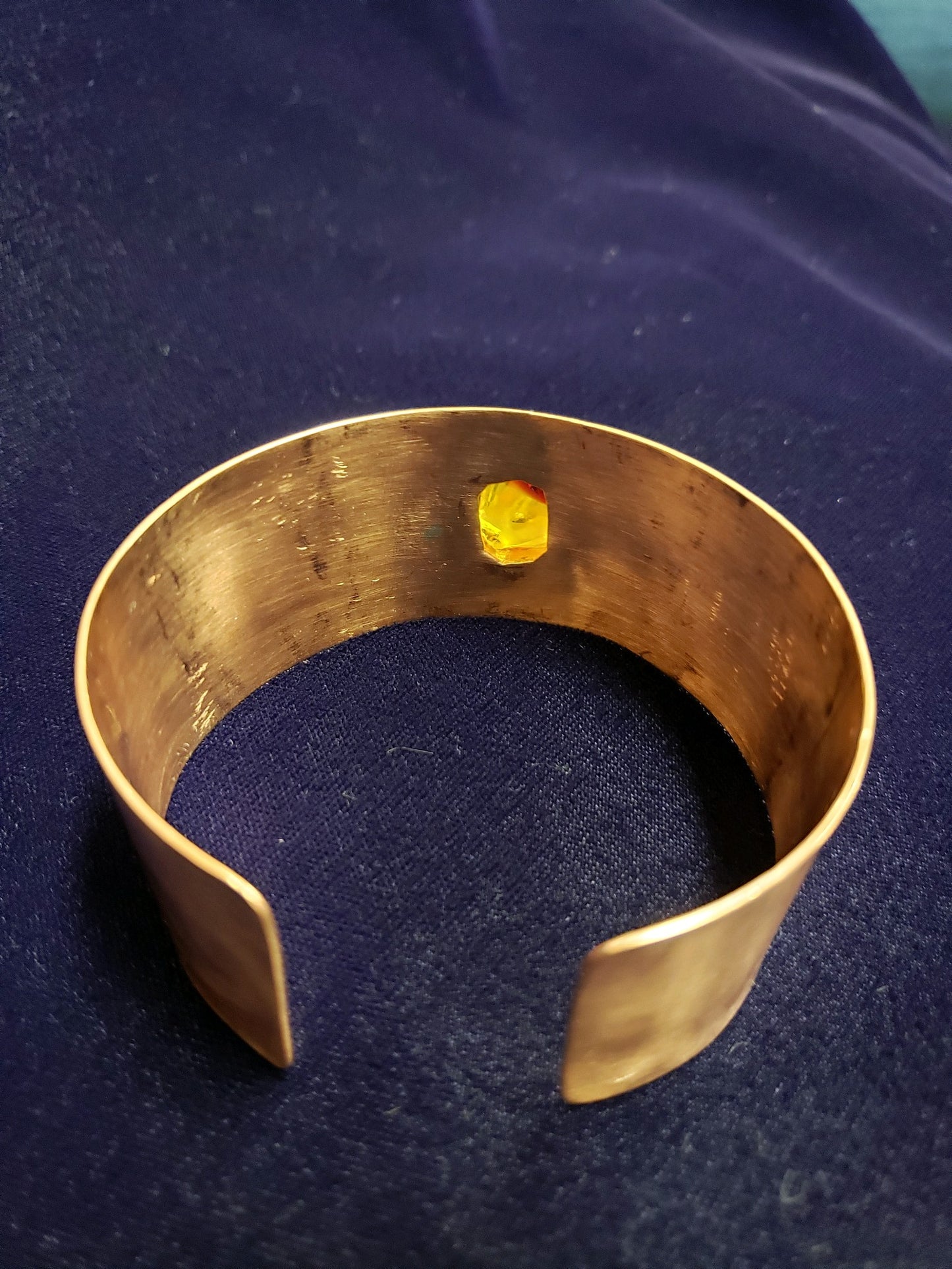 Gold bracelet with a yellow gemstone on a dark blue fabric background