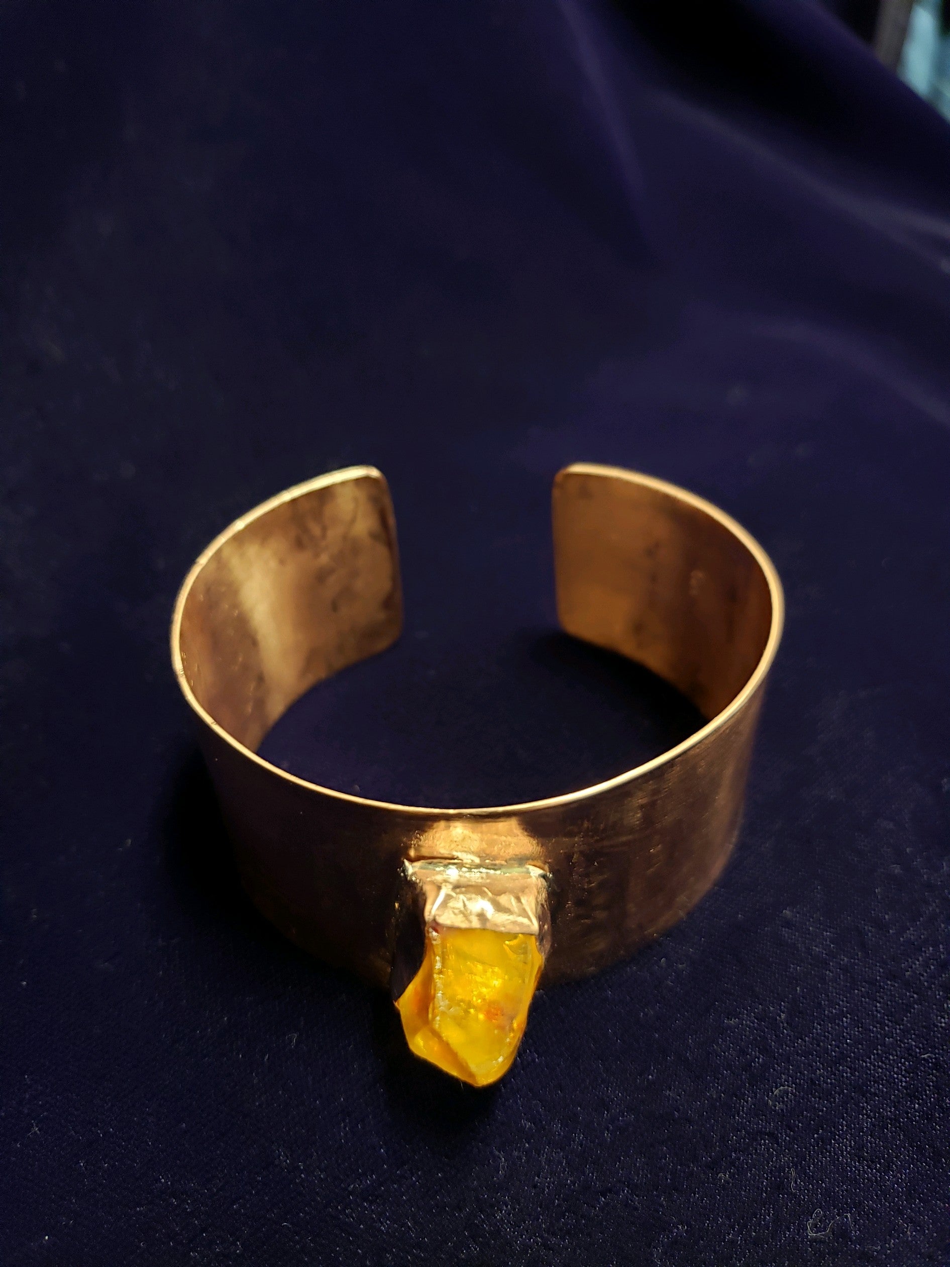 Gold bracelet with a yellow stone on a dark blue fabric background