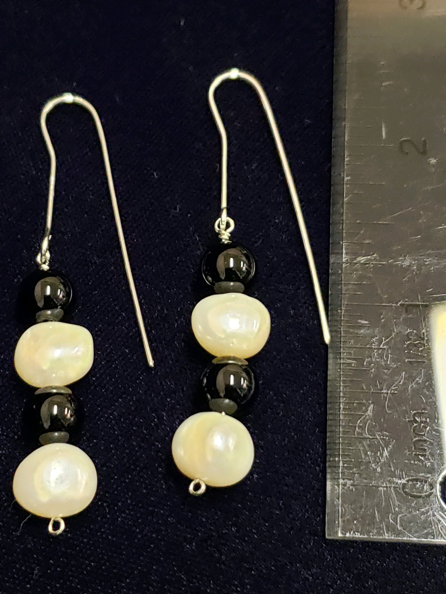 Pair of pearl and black bead earrings next to a ruler for size reference.