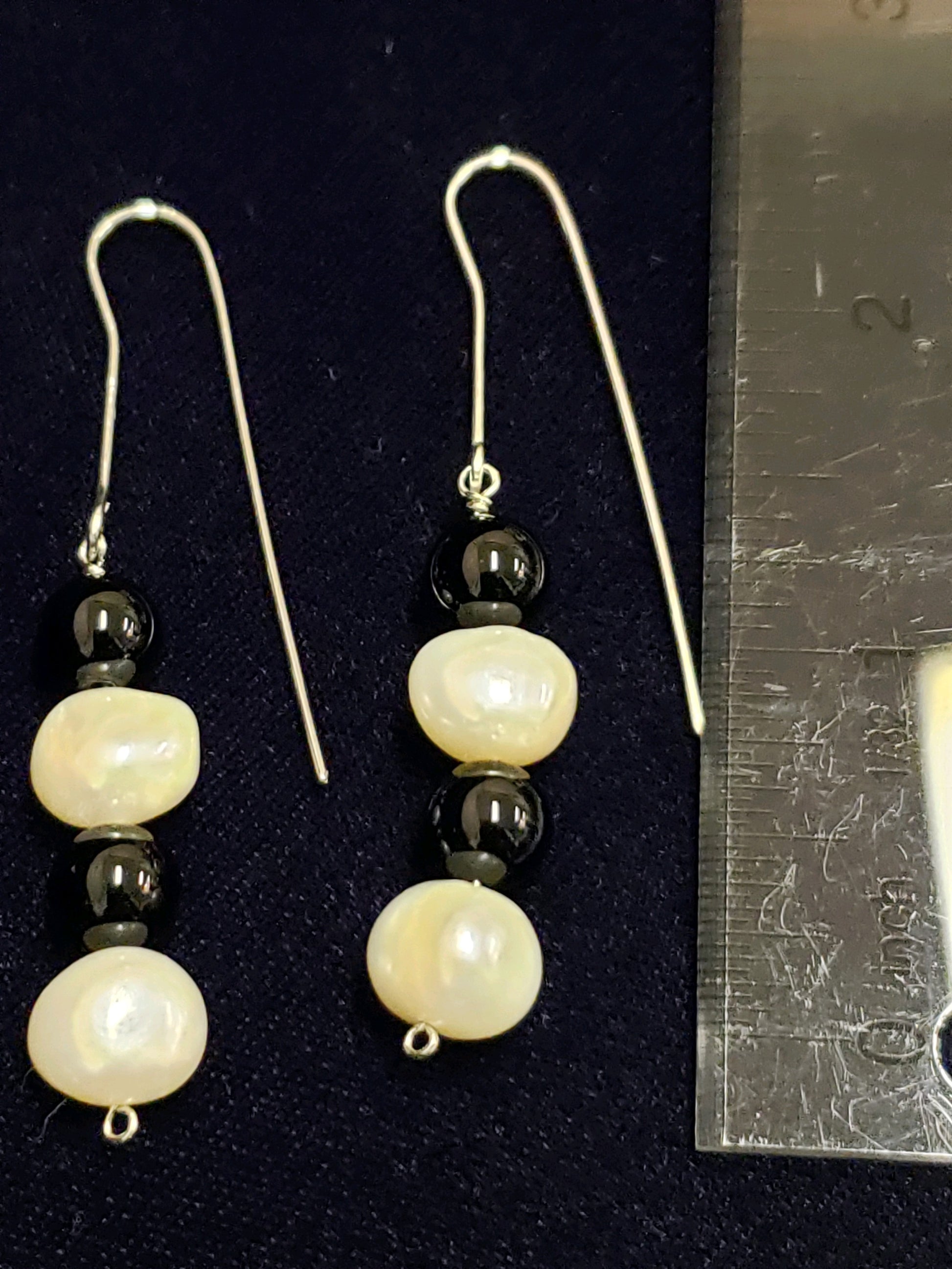 Pair of pearl and black bead earrings next to a ruler for size reference.