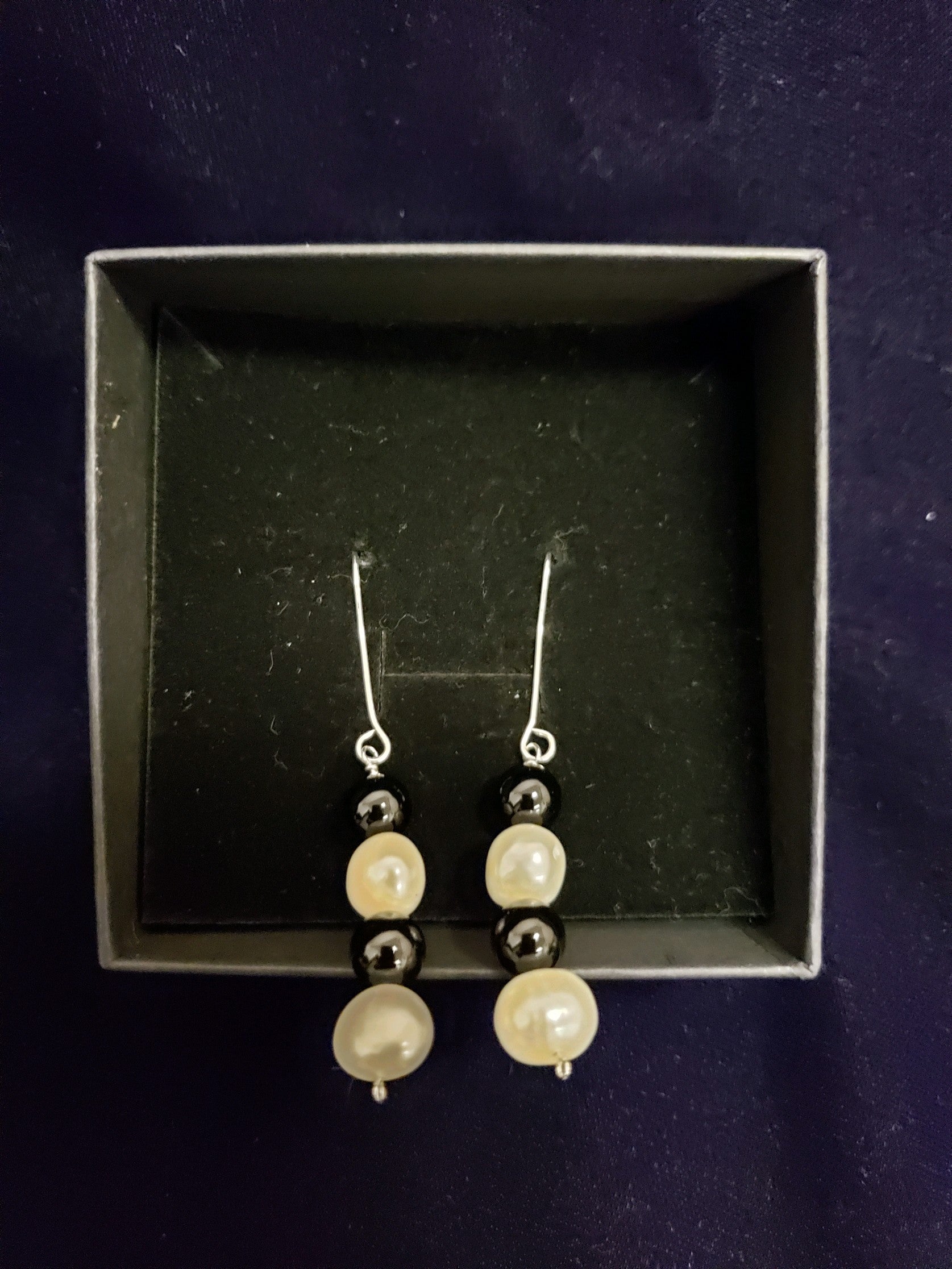 Pearl and silver earrings in a black box on a dark background