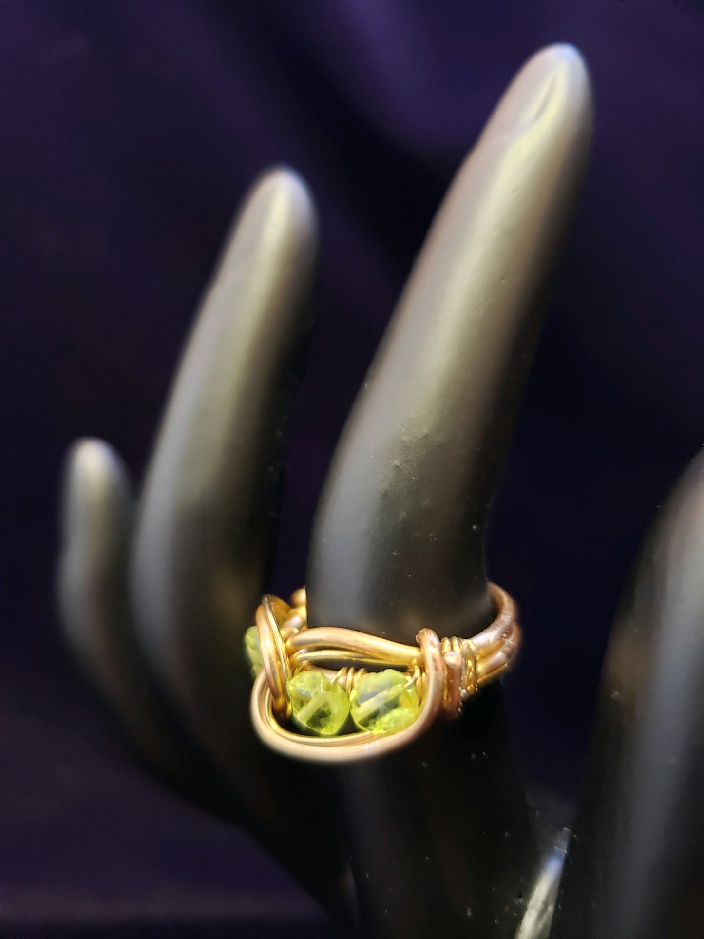 Gold ring with green gemstones on a black mannequin hand against a dark background