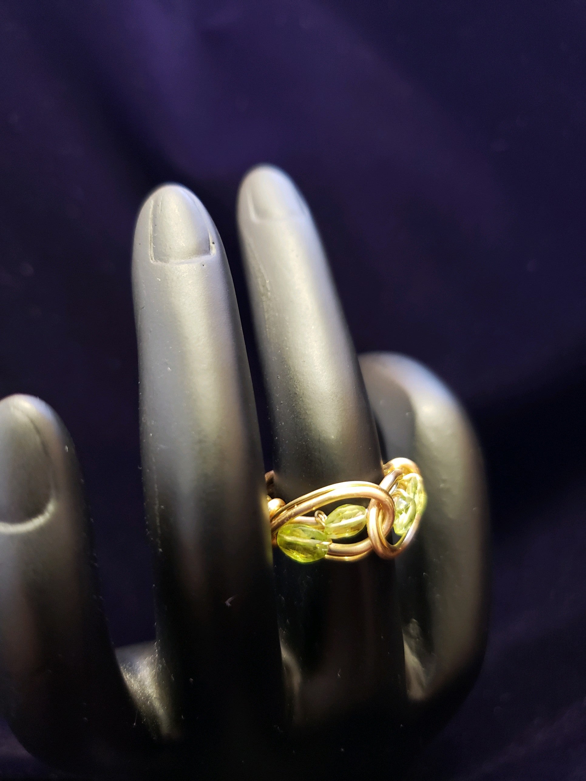 Gold ring with a green Peridot
 gemstone on a black hand model against a dark background