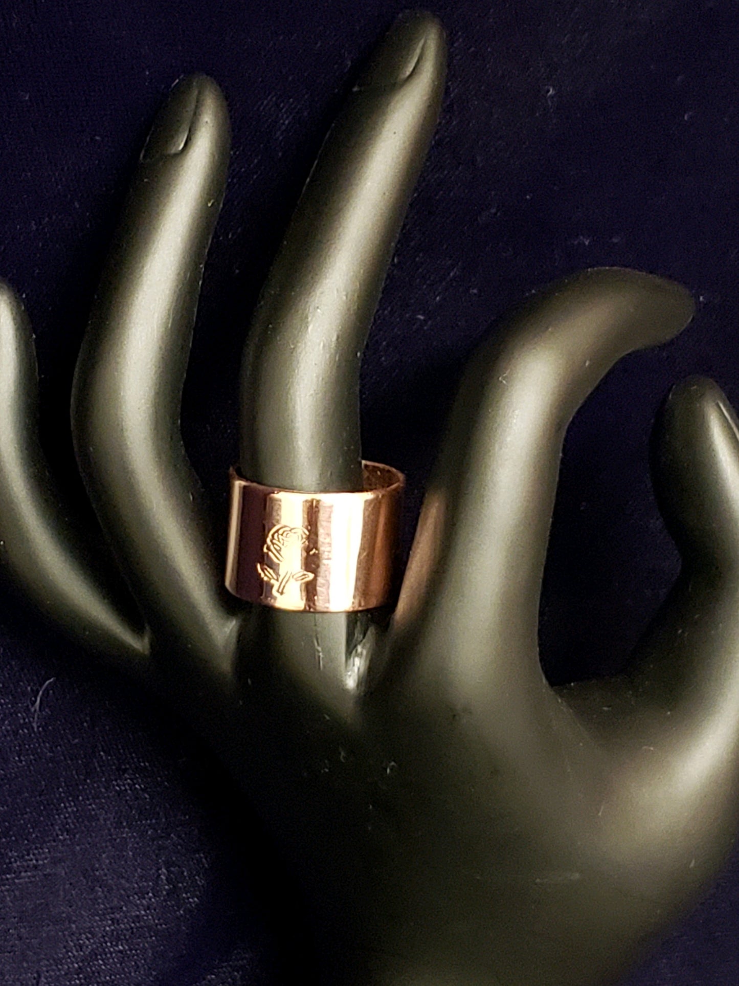 Rose gold ring on a black mannequin hand against a dark background