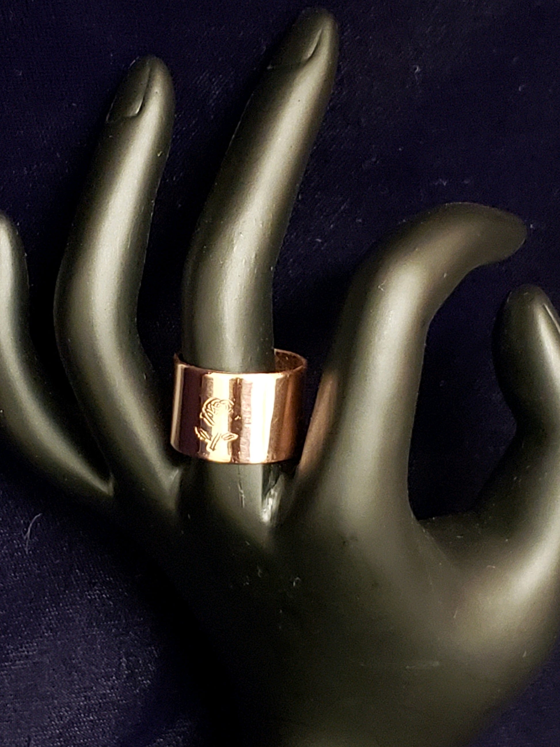 Rose gold ring on a black mannequin hand against a dark background