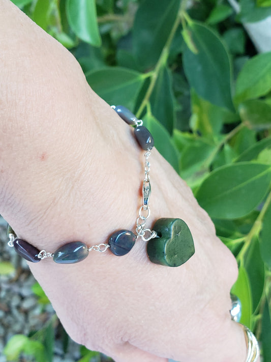 Hand- crafted bracelet with Jade and purple beads against a green leafy background