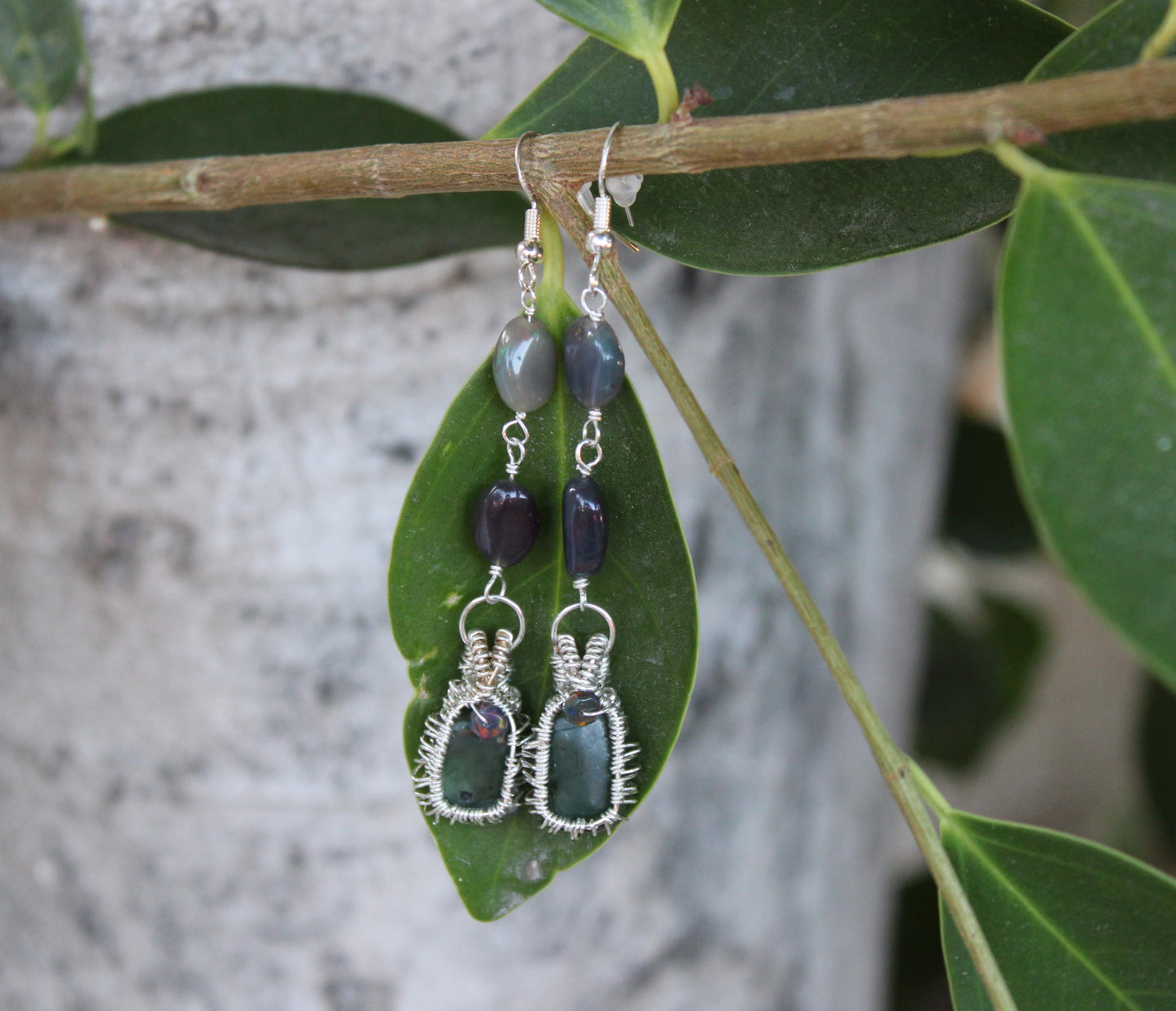 Pair of wire-wrapped earrings with Jade green and purple stones on a leaf