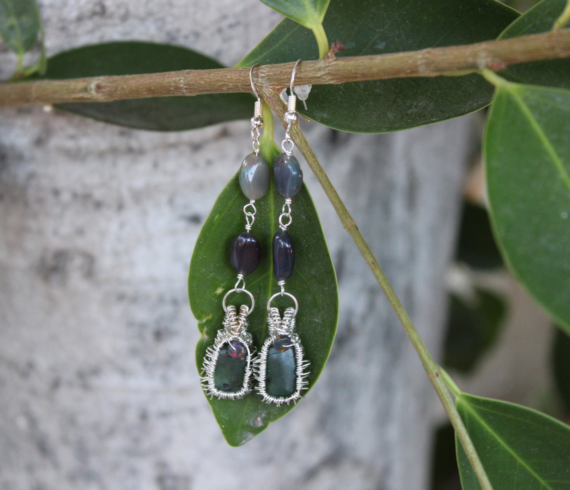 Pair of wire-wrapped earrings with Jade green and purple stones on a leaf